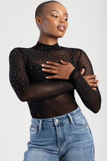 model wearing a black sheer long sleeve top with rhinestones and a high neck, paired with blue denim jeans