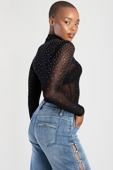 model wearing a black sheer long sleeve top with white polka dots paired with light blue jeans with a side slit by Blue