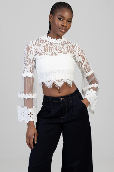 model wearing white lace cropped blouse with long sheer sleeves and high neckline, paired with dark wide leg pants