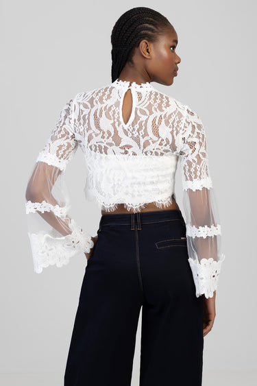 back view of a woman wearing a white lace blouse with sheer sleeves and floral trim