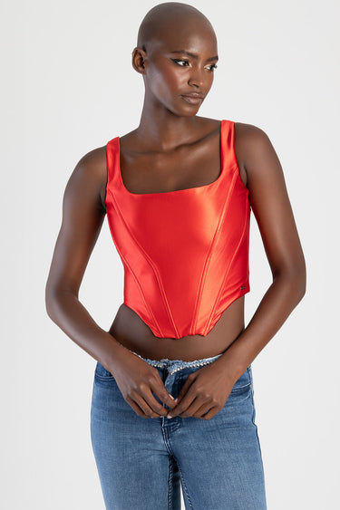 woman wearing bright red satin corset top with thick straps and seam detailing, paired with blue jeans