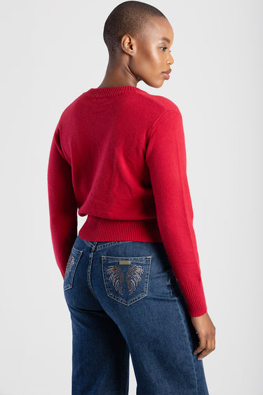 side profile of a woman wearing a red knit sweater and dark blue jeans with decorative embroidery on the back pockets