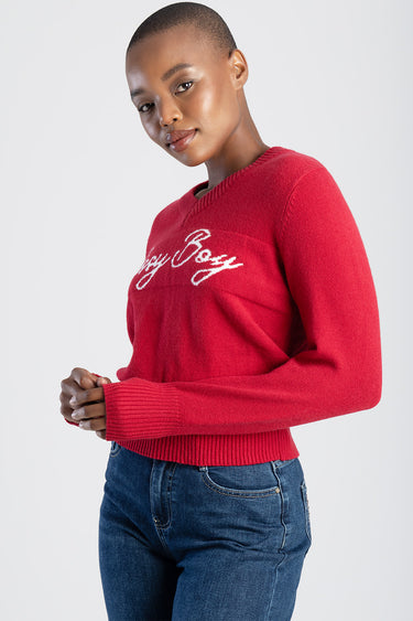 woman wearing a red knit sweater with white script logo, long sleeves with ribbed cuffs, ribbed hem, paired with blue jeans
