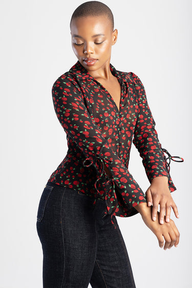 woman wearing a black sheer blouse with red rose print, deep v neck collar, long sleeves with tied cuffs, paired with dark