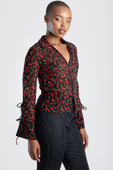 woman wearing black sheer blouse with red rose print, long sleeves with ties at cuffs, v neck wrap front, paired with dark