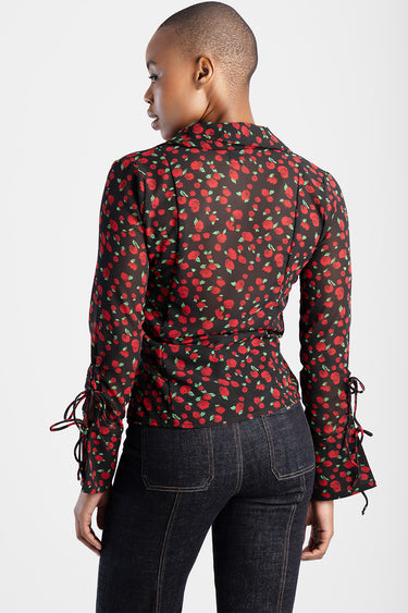 back view of black floral blouse with red rose print and tied cuffs, paired with dark denim jeans