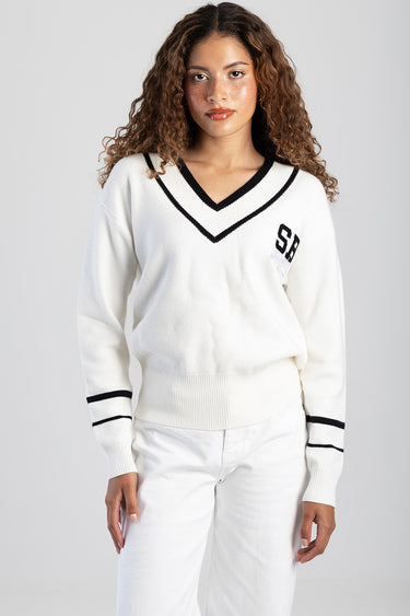 woman wearing a white knit v neck sweater with black trim and SB letters on the chest