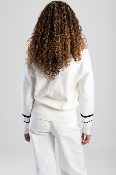 back view of a person wearing a white knit sweater with black stripe details on the sleeves and white pants