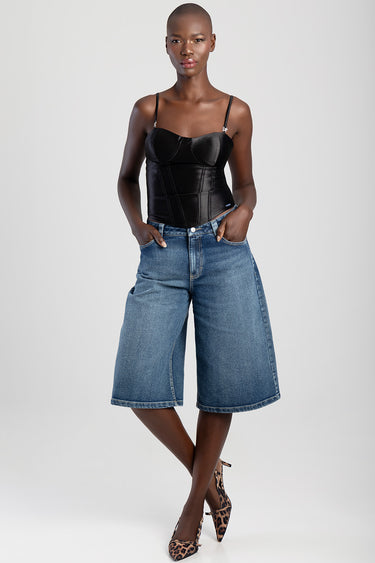 model in a black corset top with thin straps and structured cups, paired with blue denim culotte shorts and leopard print