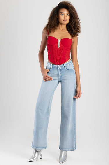 model wearing a red lace corset top with pendant detail, paired with light wash wide leg jeans and silver ankle boots