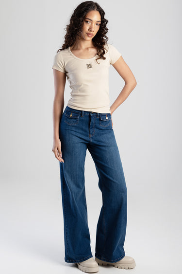 woman wearing beige ribbed short sleeve top with small logo, paired with blue wide leg jeans and tan chunky shoes