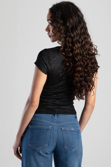 woman with long wavy hair wearing a black glitter short sleeve top and blue jeans, back view