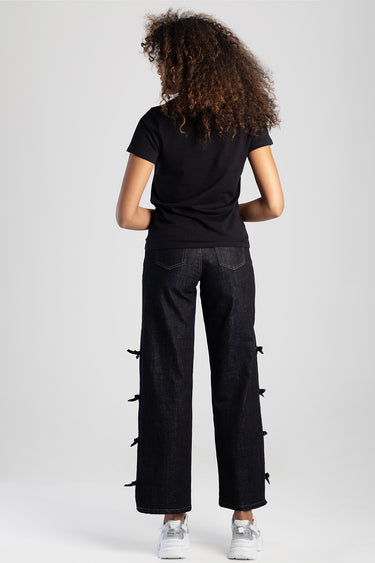 woman in a black short sleeve top and wide leg jeans with side bow details, back view, white sneakers