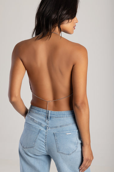 model in a backless top with a silver chain accent and light wash jeans, seen from behind