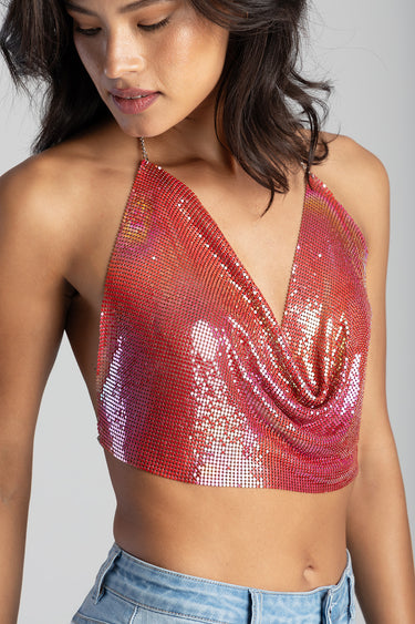 woman wearing a red sequin halter crop top with a draped neckline, paired with light blue jeans