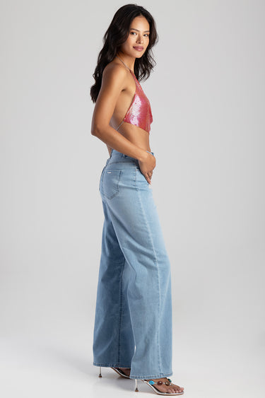 side view of a woman in a pink sequin halter crop top and light blue wide leg jeans