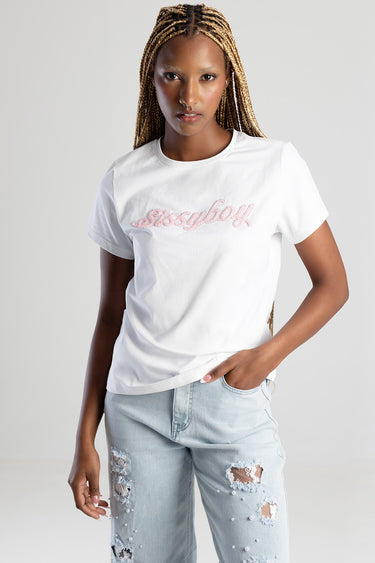 woman with long braids wearing a white short sleeve t shirt with pink cursive embroidery, paired with light wash distressed