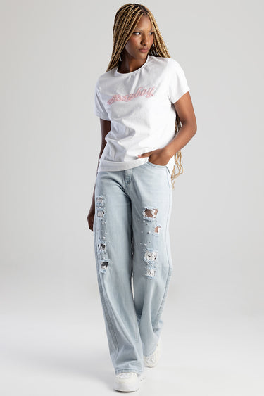 woman wearing a white short sleeve t shirt with pink script logo, light wash ripped jeans with patches and pearls, white