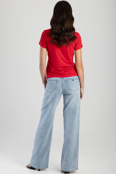 back view of a woman in a red short sleeve t shirt and light wash wide leg jeans, long dark hair