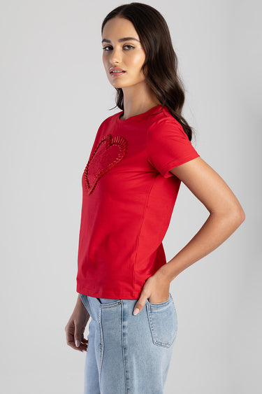 woman wearing a red short sleeve t shirt with a stitched heart graphic and light wash jeans side view
