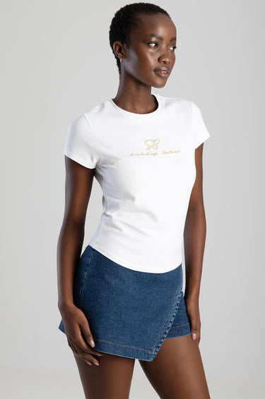 woman wearing a white short sleeve t shirt with a gold logo paired with a denim wrap mini skirt