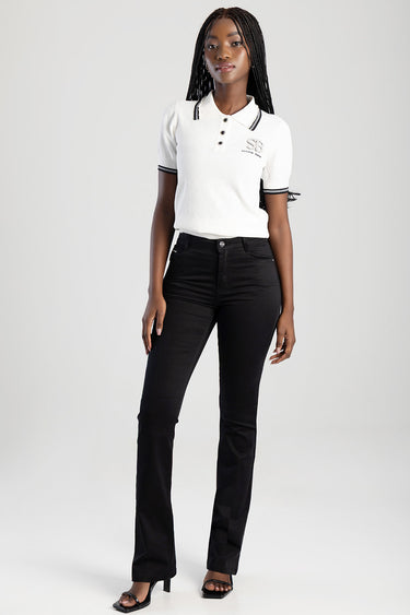 woman wearing a white knit polo with black striped collar and sleeve trim, black jeans, and heeled sandals