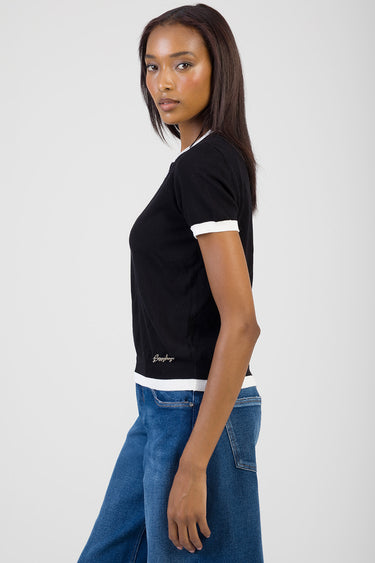 woman wearing a black knit top with white ribbed trim on sleeves and hem, side profile view with a small logo embroidery