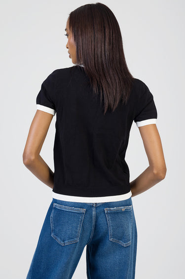 back view of a woman in a black knit top with white cuffs and hem, paired with blue jeans.