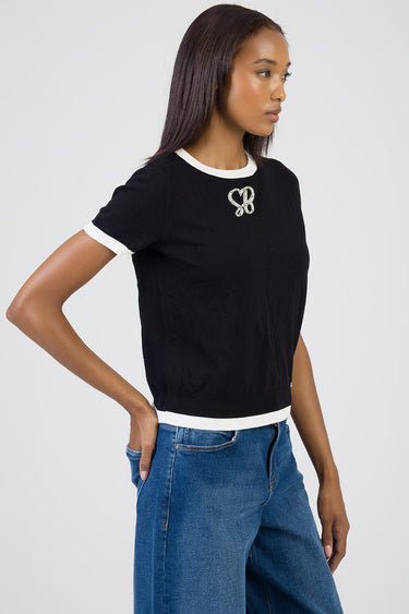 model wearing blue jean traders black knit top with white crew neck and hem trim and a rhinestone chest logo