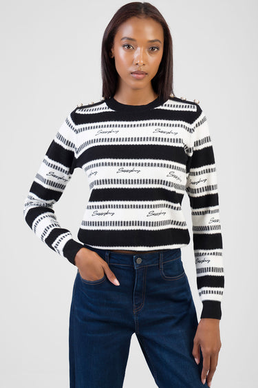 woman wearing a black and white striped knit sweater with shoulder buttons, paired with dark jeans