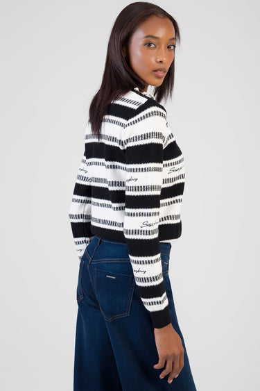 woman in black and white striped knit sweater and dark blue jeans, shown in side profile