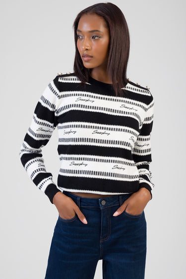 model wearing a black and white striped knit sweater with shoulder buttons and script logo across the stripes, paired with