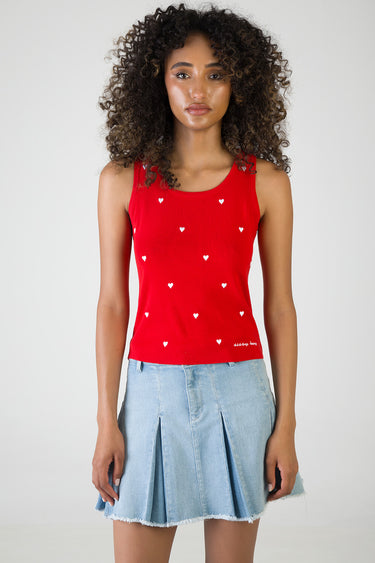 woman wearing a red sleeveless knit top with white heart prints and a light blue pleated denim mini skirt