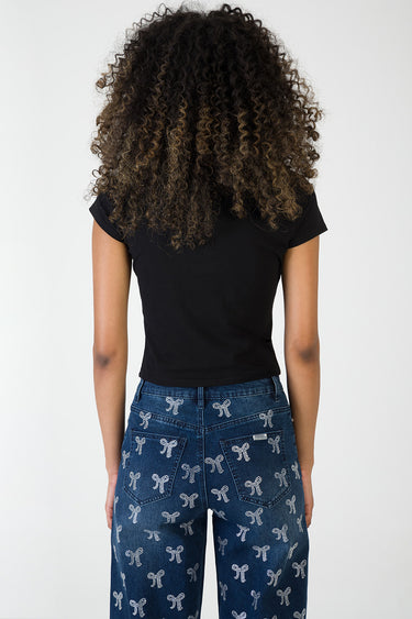 back view of a person wearing a black short sleeve top and blue jeans with a white bow pattern
