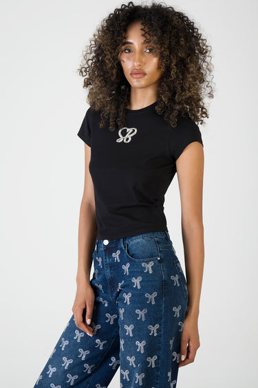 woman wearing a black short sleeve t shirt with a crystal bow logo, paired with blue jeans covered in small white bows