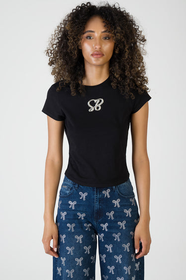 woman wearing a black short sleeve t shirt with rhinestone initials on the chest and blue jeans with a white bow pattern
