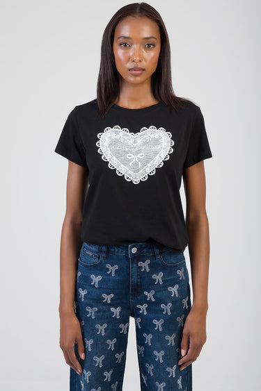 woman wearing a black short sleeve t shirt with a white lace heart design on the front paired with blue jeans featuring a