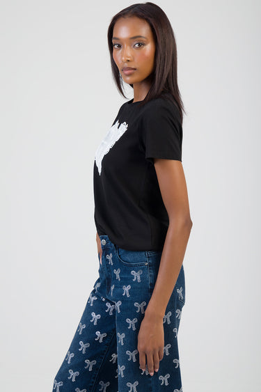 woman wearing black short sleeve t shirt with white graphic, blue jeans with white bow print, side view.