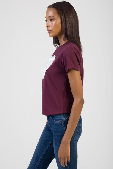 woman in a maroon short sleeve t shirt with a white graphic on the chest, side view, blue jeans