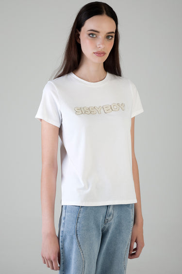 woman wearing a white short sleeve t shirt with a pearl embellished logo on the chest and light wash jeans