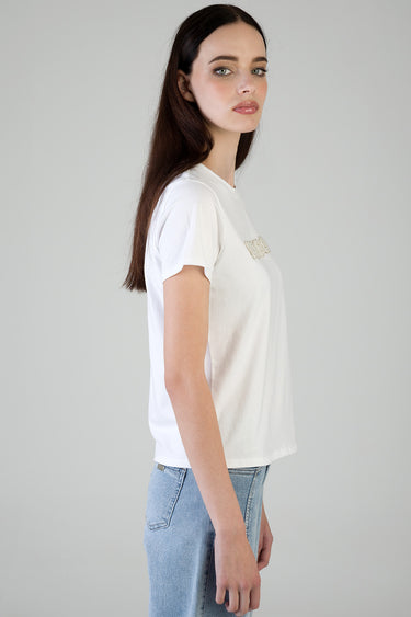 side view of a woman wearing a white short sleeve t shirt with a small rhinestone patch on the chest, paired with light