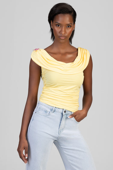 woman wearing a yellow draped top with ruching at the sides and a sparkly pin on the left shoulder, paired with light wash