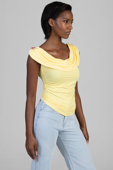 woman in yellow draped neck top with ruched sides paired with light wash jeans, posing in profile