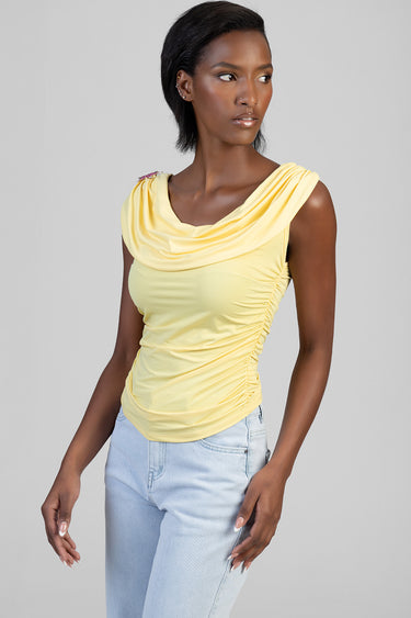 woman modeling a pale yellow draped sleeveless top with ruching at the sides and light blue jeans