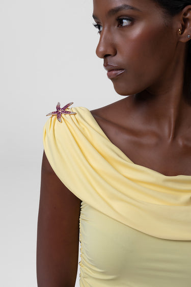 close up of a woman in a pale yellow one shoulder top with a jeweled starfish brooch on the shoulder