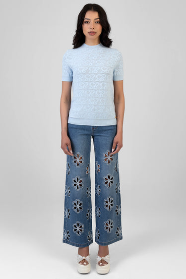 woman in light blue lace knit top with short sleeves and ribbed hem, paired with wide leg jeans featuring floral cutout
