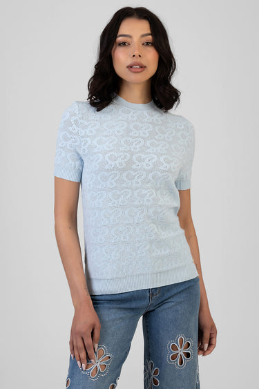 woman wearing a light blue knit top with short sleeves and a floral lace pattern