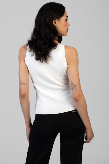 woman in white sleeveless knit top and black pants, shown from the back, with tattoos on arms