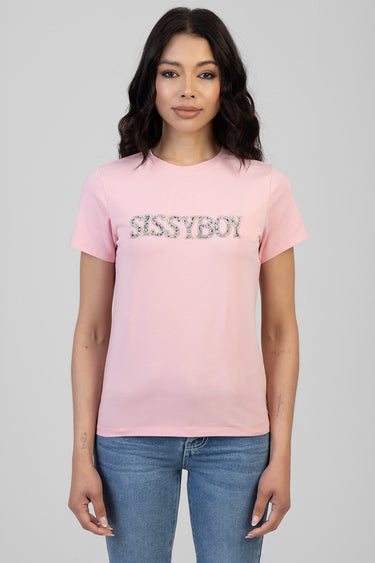 woman wearing a light pink short sleeve t shirt with a rhinestone logo across the chest and blue jeans