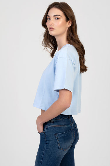 woman in light blue boxy short sleeve t shirt standing in profile with jeans
